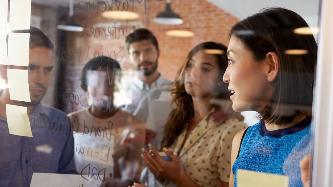 Um grupo de pessoas em pé em frente a um quadro com notas adesivas.